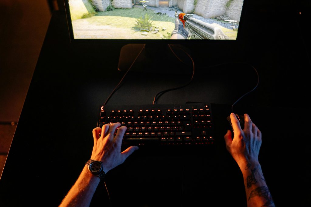 A gamer intensely playing a first-person shooter game on a computer setup indoors at night.